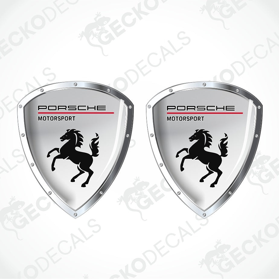 Two Porsche Motorsport shield-shaped decals with a silver metallic border, black horse logo, and red accent line on a white background.