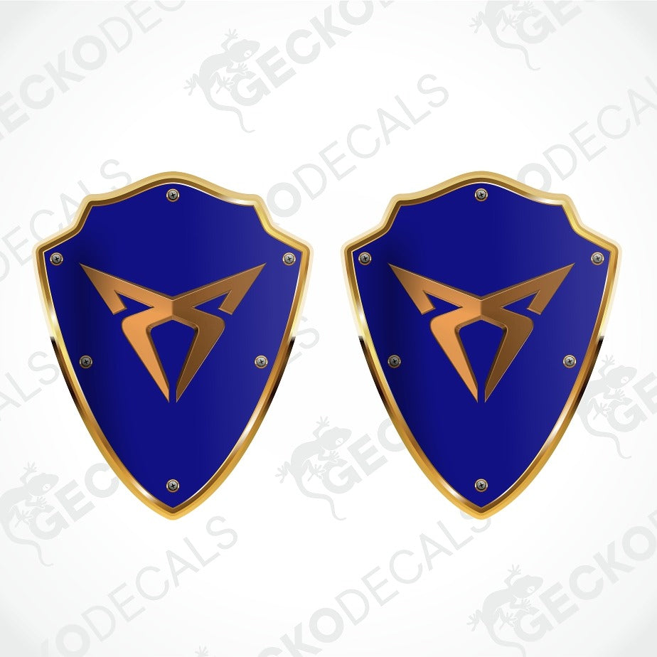 Two identical blue and gold shield-shaped decals with a stylized gold emblem in the center, shown on a white background with a faint diagonal watermark pattern.