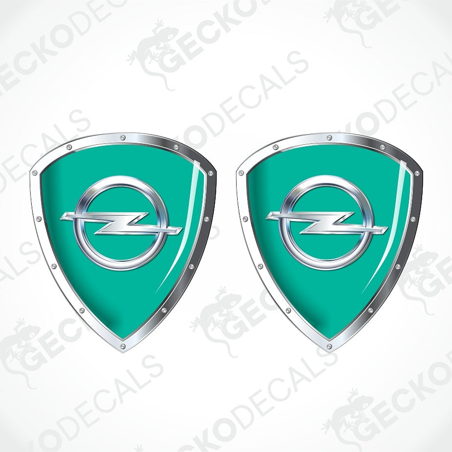Two identical teal and silver shield-shaped decals with the Opel logo in the center, shown on a light gray background with diagonal watermark text.