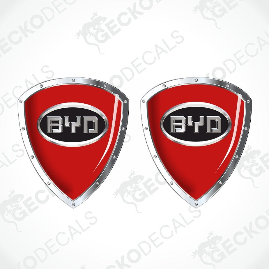 Two red shield-shaped BYD car decals with silver metallic borders and a black center containing the BYD logo, shown on a white background with faint watermarks.