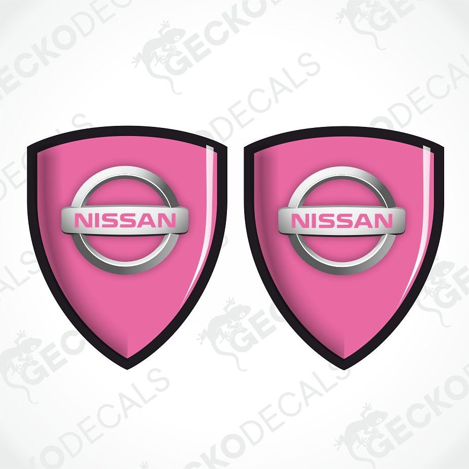 Two pink Nissan shield-shaped decals with the silver and pink Nissan logo in the center, shown on a white background with a faint watermark pattern.