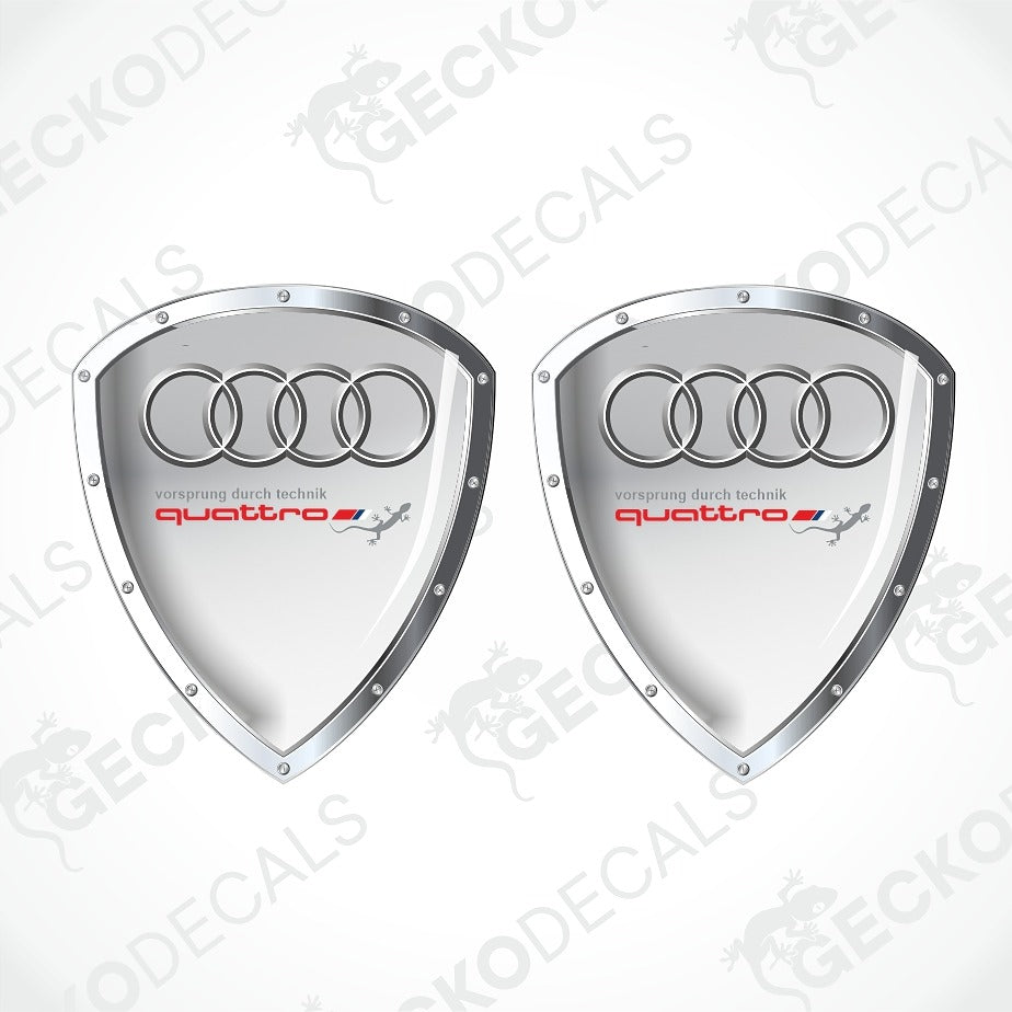 Two silver shield-shaped Audi quattro decal stickers on a white background with diagonal watermarks.