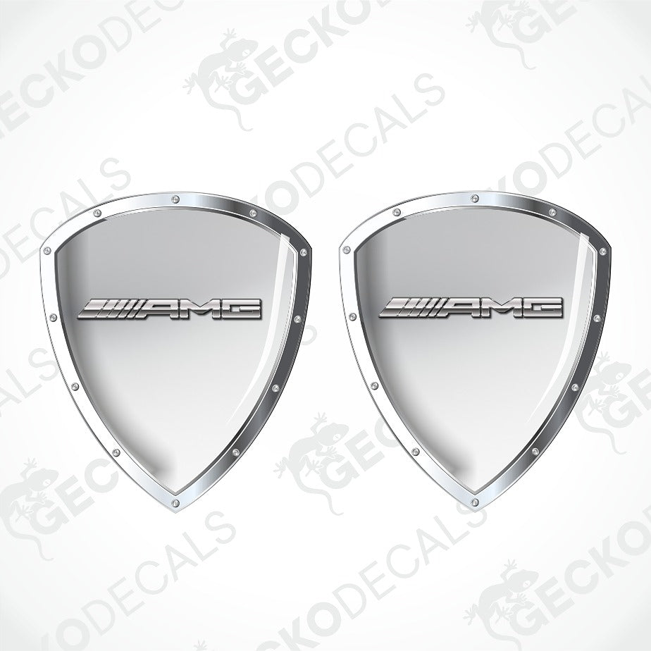 A pair of silver Mercedes-AMG shield-shaped decals with the AMG logo in the center, displayed on a light gray background with diagonal watermarks.