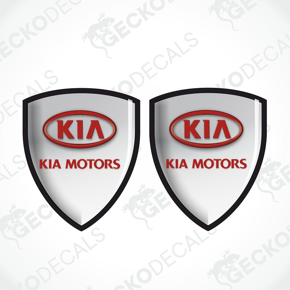 Two identical shield-shaped Kia Motors decals on a light gray background with diagonal watermarks. Each shield has a black border, a white center, a red oval Kia logo, and red 'KIA MOTORS' text.