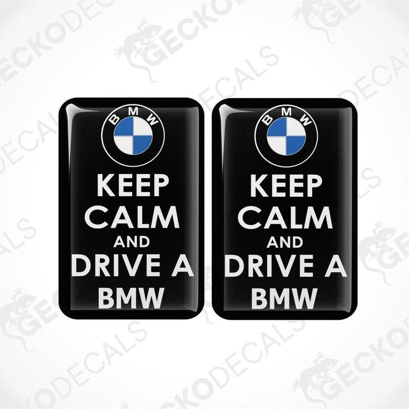 Two rectangular black vinyl decals with the text 'KEEP CALM AND DRIVE A BMW' in white, and the BMW logo in blue and white.