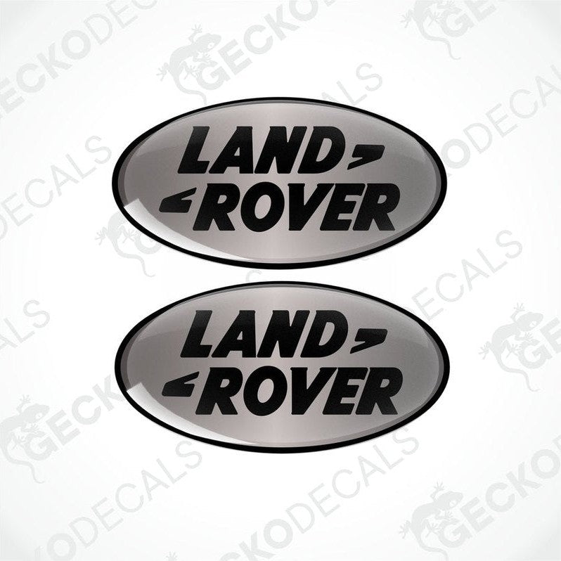 Two oval-shaped black and silver vinyl decals with the text 'LAND ROVER' on them.