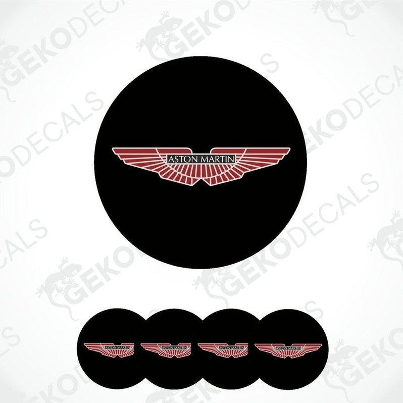 A set of vinyl decals with the Aston Martin logo applied on black circular surfaces, likely for vehicle wheels.