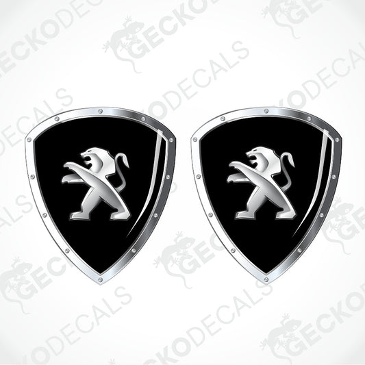 Two identical shield-shaped decals featuring the Peugeot lion logo in silver on a black background, with a chrome silver border and rivet details, shown on a light gray background with a faint watermark pattern.