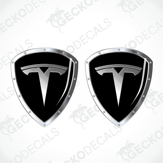 Two black and silver Tesla shield-shaped decals with the Tesla logo, shown on a light gray background with diagonal watermark text.