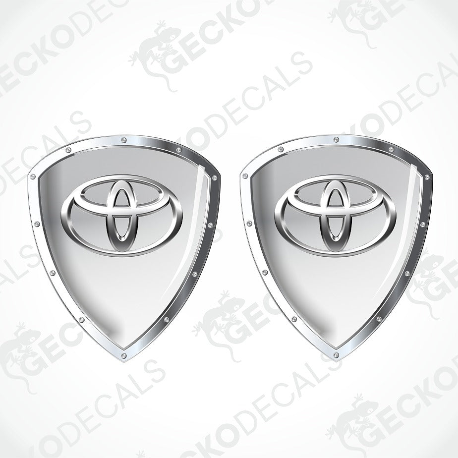 Two identical silver shield-shaped decals featuring the Toyota logo, displayed side-by-side on a light gray background with diagonal watermarks.