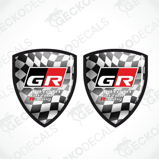 Two identical shield-shaped Toyota Gazoo Racing decals on a light gray background with diagonal watermarks. Each decal features a black and white checkered pattern, a central black and red square with white 'GR' lettering, and 'TOYOTA GAZOO Racing' written below.