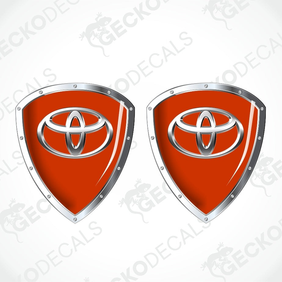Two identical red shield-shaped decals with silver metallic borders and a silver Toyota emblem in the center, shown on a light gray background with repeated GECKODECALS watermarks.