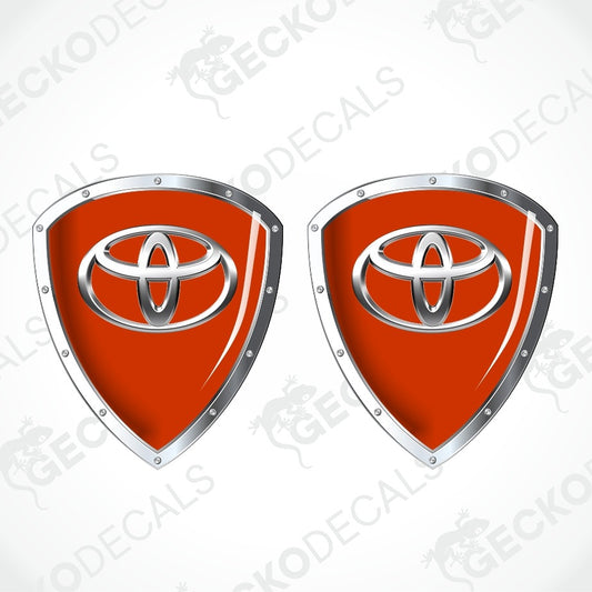 Two identical red shield-shaped decals with silver metallic borders and a silver Toyota emblem in the center, shown on a light gray background with repeated GECKODECALS watermarks.