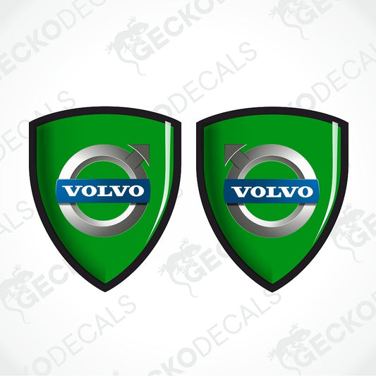 Two green Volvo shield-shaped decals with black borders, a silver circular emblem, and a blue Volvo logo bar, shown on a light gray background with faint watermark text.