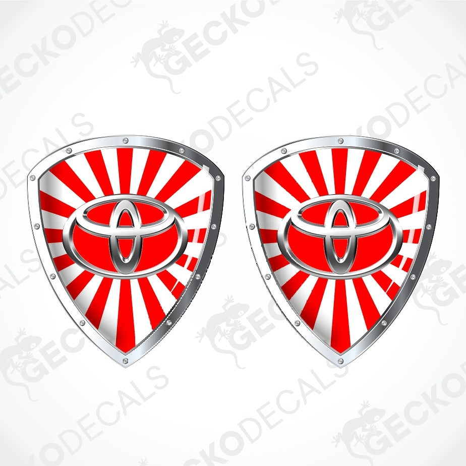 Two identical shield-shaped decals featuring the red and white Toyota logo over a red and white sunburst background, with silver metallic borders, shown on a light gray background with a faint GECKODECALS watermark.