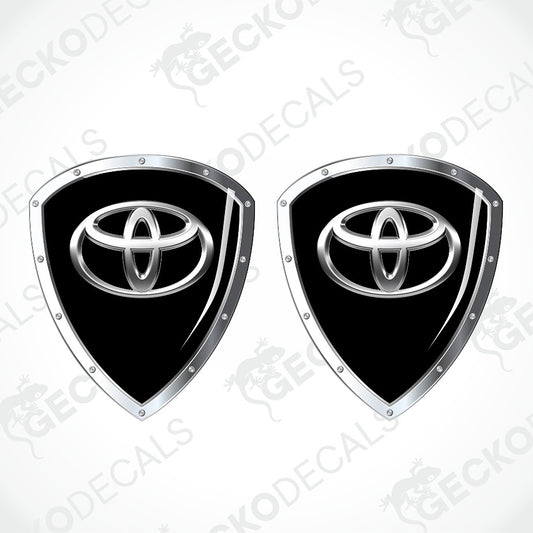 Two identical black and silver Toyota shield-shaped decals on a light gray background with diagonal watermarks.