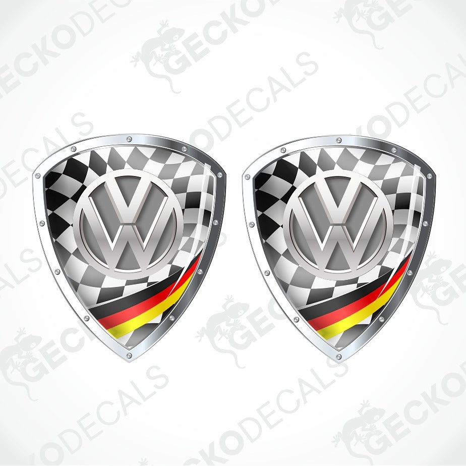Two identical Volkswagen shield-shaped decals on a light gray background. Each decal features a black-and-white checkered pattern, a metallic silver VW logo, and a diagonal German flag stripe in black, red, and yellow.