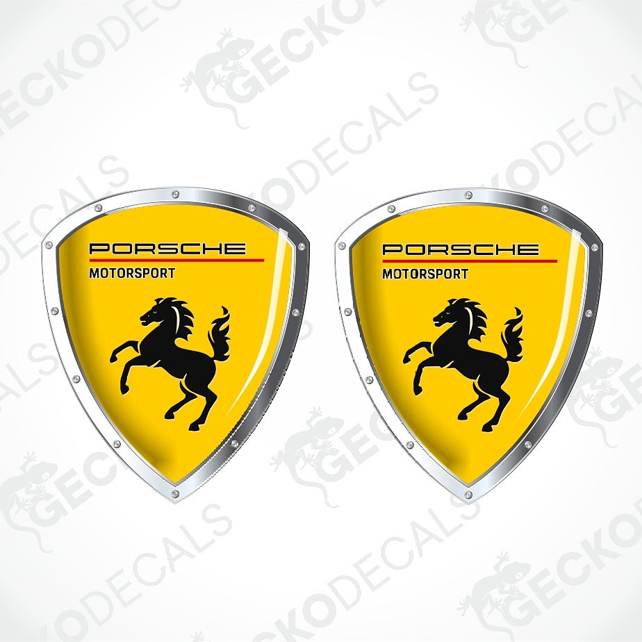 Two Porsche Motorsport shield-shaped decals with a bright yellow background, black horse logo, and silver border on a white background with faint watermark text.