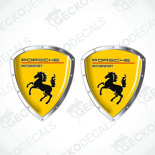 Two Porsche Motorsport shield-shaped decals with a bright yellow background, black horse logo, and silver border on a white background with faint watermark text.