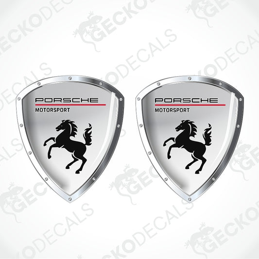 Two Porsche Motorsport shield-shaped decals with a silver metallic border, black horse logo, and red accent line on a white background.