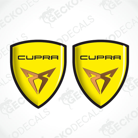 Two identical yellow shield-shaped decals with black outlines, the word 'CUPRA' in black at the top, and a stylized brown logo below, shown on a light gray background with faint diagonal watermarks.