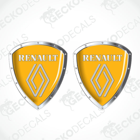 Two Renault shield-shaped decals with a glossy yellow face, silver metallic borders, and the Renault wordmark and logo, shown on a light gray background with faint watermark text.
