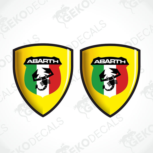 Two identical Abarth shield decals on a white background with faint watermark text. Each shield has a yellow border, a black Abarth logo, and a green, white, and red vertical tricolor design.