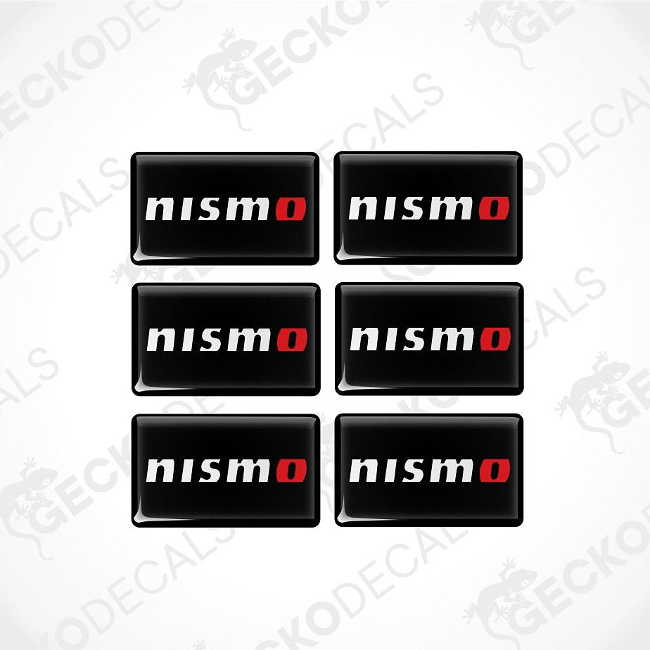 Six black rectangular decals with rounded corners, arranged in a 2x3 grid on a light gray background. Each decal features the word 'nismo' in white with a red 'o' accent.