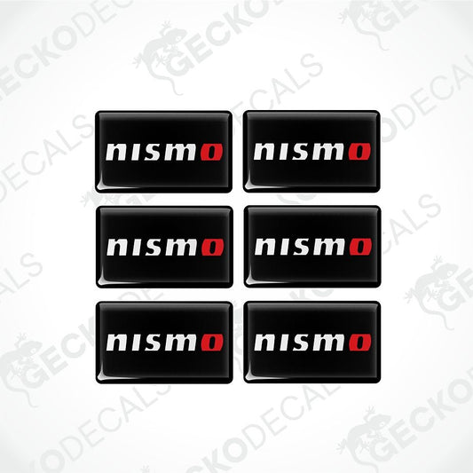 Six black rectangular decals with rounded corners, arranged in a 2x3 grid on a light gray background. Each decal features the word 'nismo' in white with a red 'o' accent.