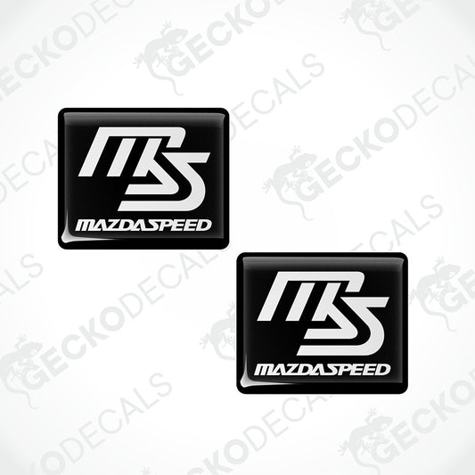 Two black rectangular decals with rounded corners featuring a stylized white 'MBS' logo and the text 'MAZDASPEED' on a light gray background with faint watermarks.