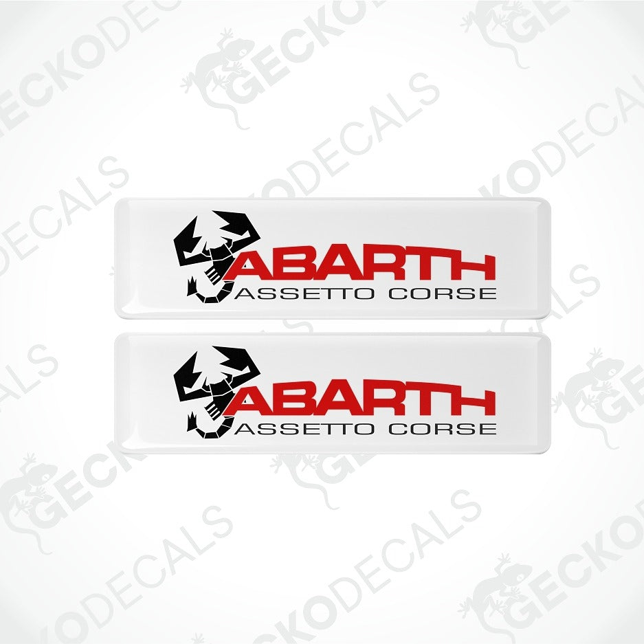 Two rectangular Abarth Assetto Corse decals stacked vertically on a light gray background. The decals are white with a black wolf logo and red and black text.