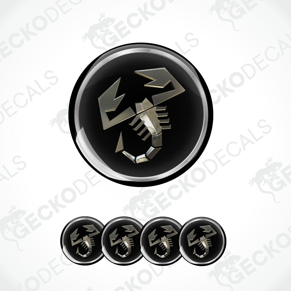 A circular black decal or sticker featuring a metallic silver scorpion symbol, shown with four smaller identical decals aligned horizontally below on a white background with faint watermark text.