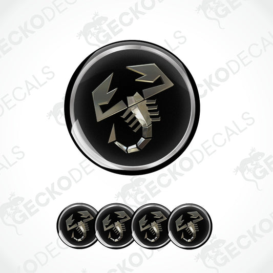 A circular black decal or sticker featuring a metallic silver scorpion symbol, shown with four smaller identical decals aligned horizontally below on a white background with faint watermark text.