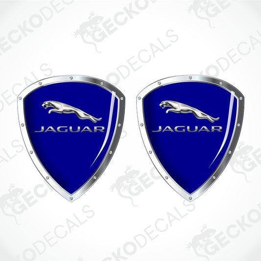 Two identical Jaguar shield-shaped decals on a light gray background with diagonal watermarks. Each decal has a glossy royal blue center, silver border, silver Jaguar leaping cat logo, and silver JAGUAR text.