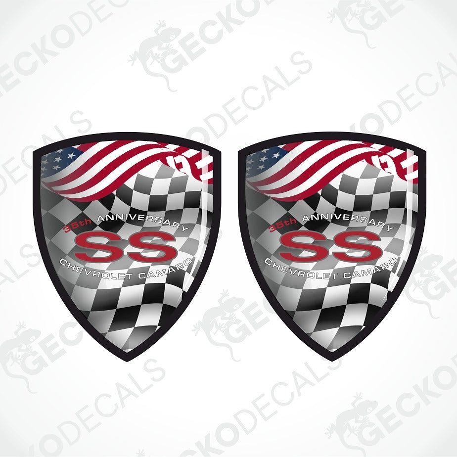 Two matching shield-shaped decals on a light gray background. Each shield features a black-and-white checkered lower section, a waving American flag across the top, and large red 'SS' lettering with smaller white text reading '50th Anniversary' and 'Chevrolet Camaro.