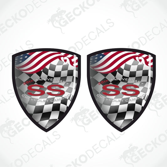 Two matching shield-shaped decals on a light gray background. Each shield features a black-and-white checkered lower section, a waving American flag across the top, and large red 'SS' lettering with smaller white text reading '50th Anniversary' and 'Chevrolet Camaro.