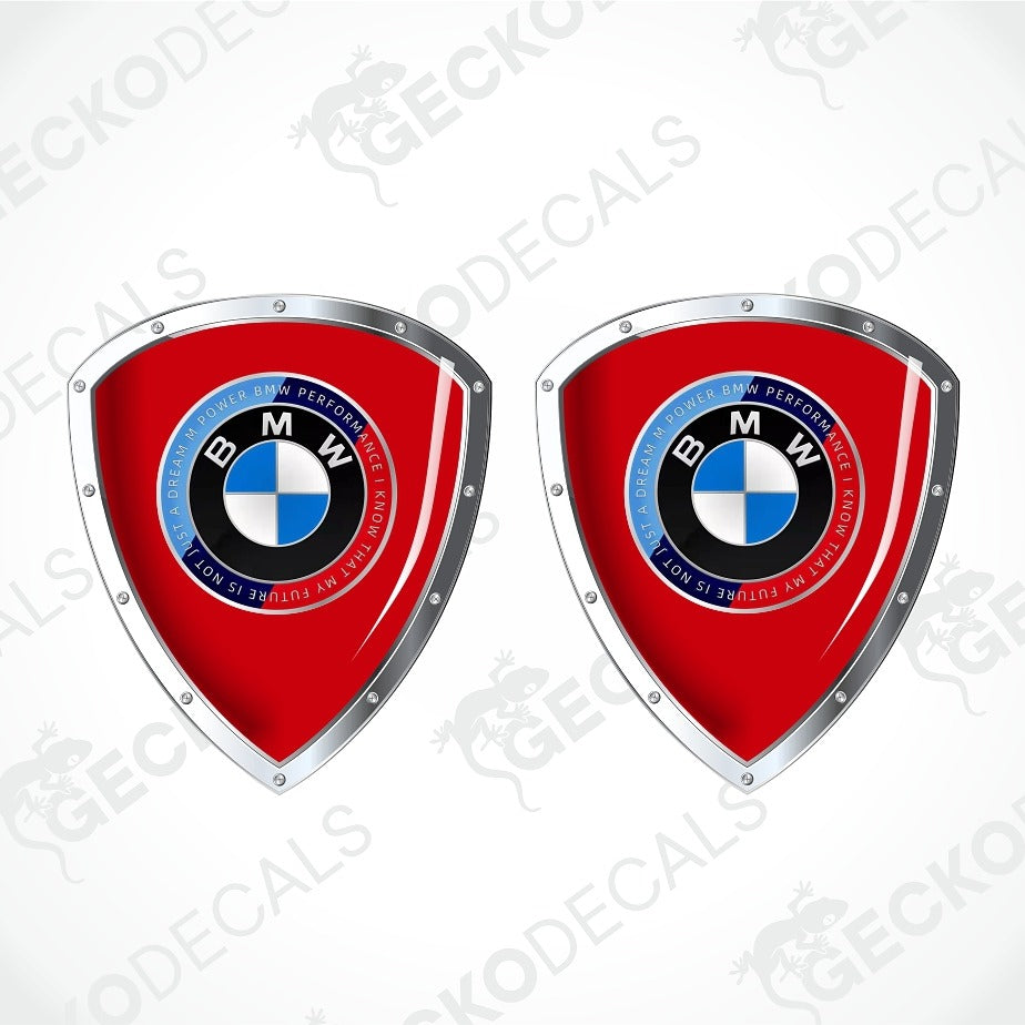 Two red shield-shaped BMW decal designs with silver metallic borders and the BMW roundel logo in the center, shown on a light gray background with faint GECKODECS watermarks.