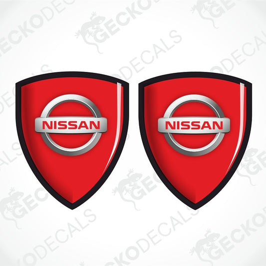 Two red Nissan shield-shaped decals with black borders and silver Nissan logos, shown on a white background with a faint watermark pattern.