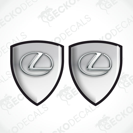 Two identical Lexus shield-shaped decals with a glossy silver and white gradient center, a black border, and the silver Lexus logo in the middle, shown on a light gray background with faint Geckodec watermarks.
