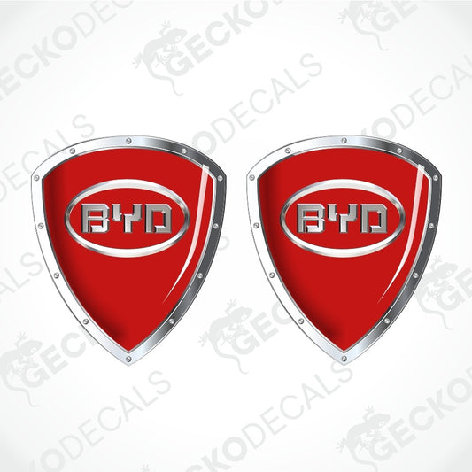 Two red shield-shaped decal emblems with silver metallic borders and the BYD logo in the center, shown on a light gray background with faint diagonal watermarks.