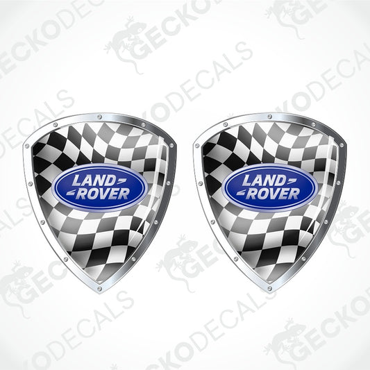 Two Land Rover shield-shaped decals with a black and white checkered flag pattern and a blue oval Land Rover logo in the center, shown on a light gray background with faint watermark text.