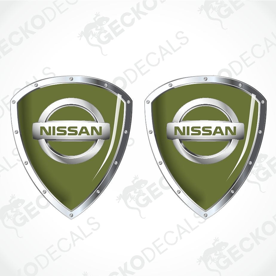 Two identical Nissan shield-shaped decals on a white background with diagonal watermark text. The decals feature an olive green center with a silver metallic border and a silver horizontal bar displaying the NISSAN logo.