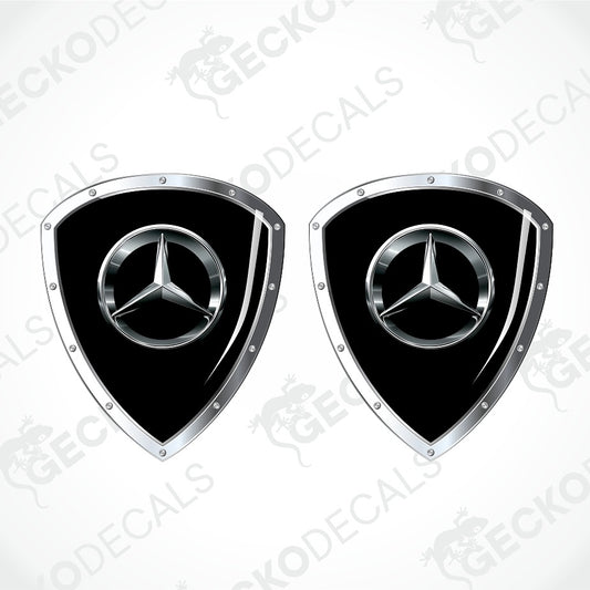 Two Mercedes-Benz shield-shaped decals with a glossy black center and a silver metallic three-pointed star logo, shown on a light gray background with faint watermark text.