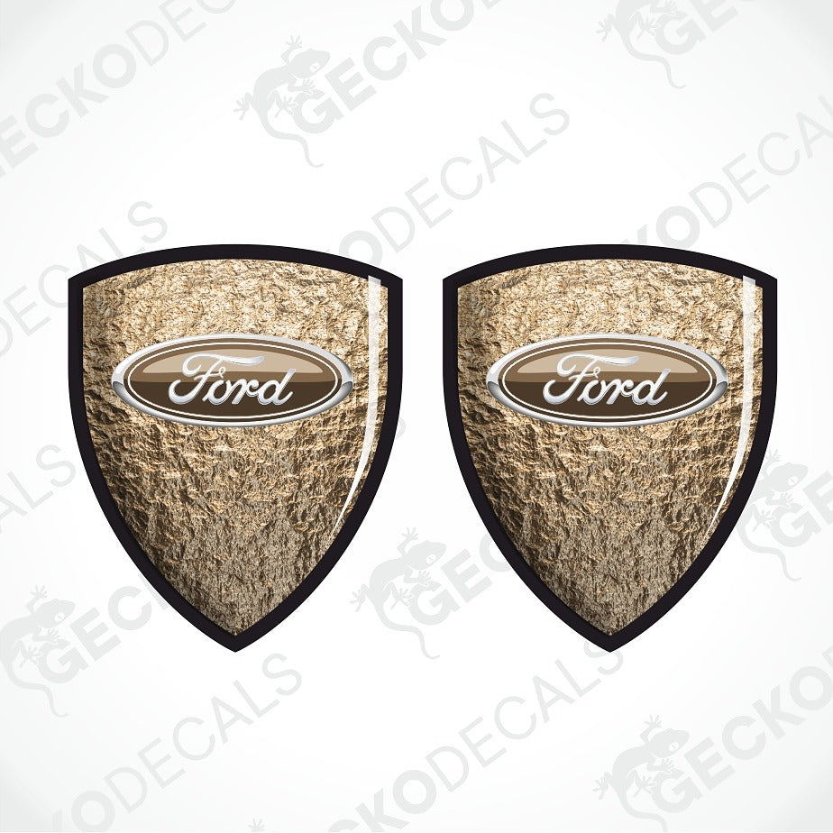 Two Ford shield-shaped decals with a textured metallic gold background, black borders, and a central oval Ford logo, shown on a white background with a faint GECKODECALS watermark.