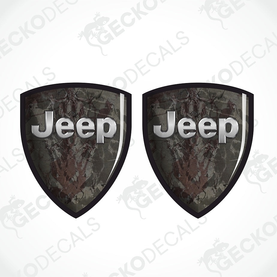 Two shield-shaped Jeep decals with a dark camouflage pattern and raised silver 'Jeep' lettering, shown on a white background with a faint watermark.