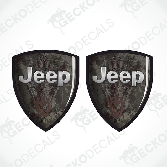 Two shield-shaped Jeep decals with a dark camouflage pattern and raised silver 'Jeep' lettering, shown on a white background with a faint watermark.