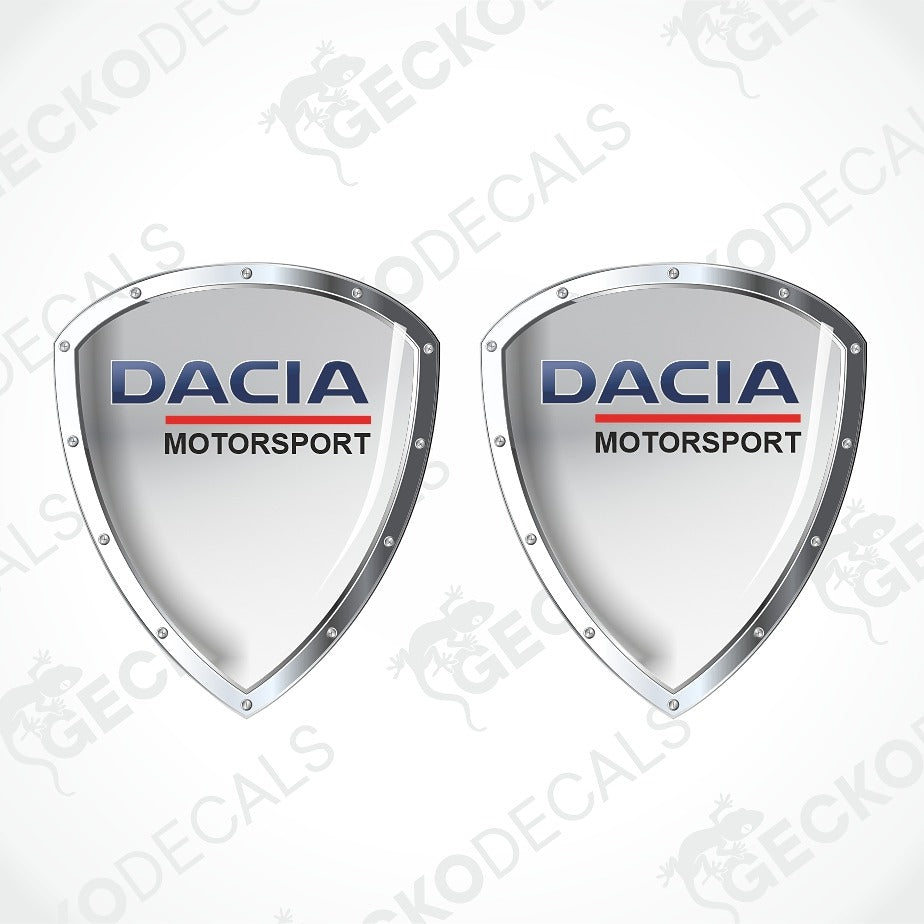 Two identical Dacia Motorsport shield-shaped decals on a white background with diagonal watermarks. The decals feature a light mint green center, silver metallic borders, and the Dacia Motorsport logo in blue and red.