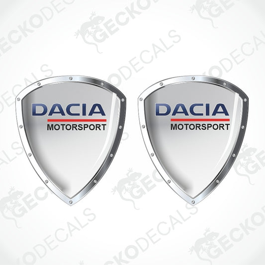 Two identical Dacia Motorsport shield-shaped decals on a white background with diagonal watermarks. The decals feature a light mint green center, silver metallic borders, and the Dacia Motorsport logo in blue and red.