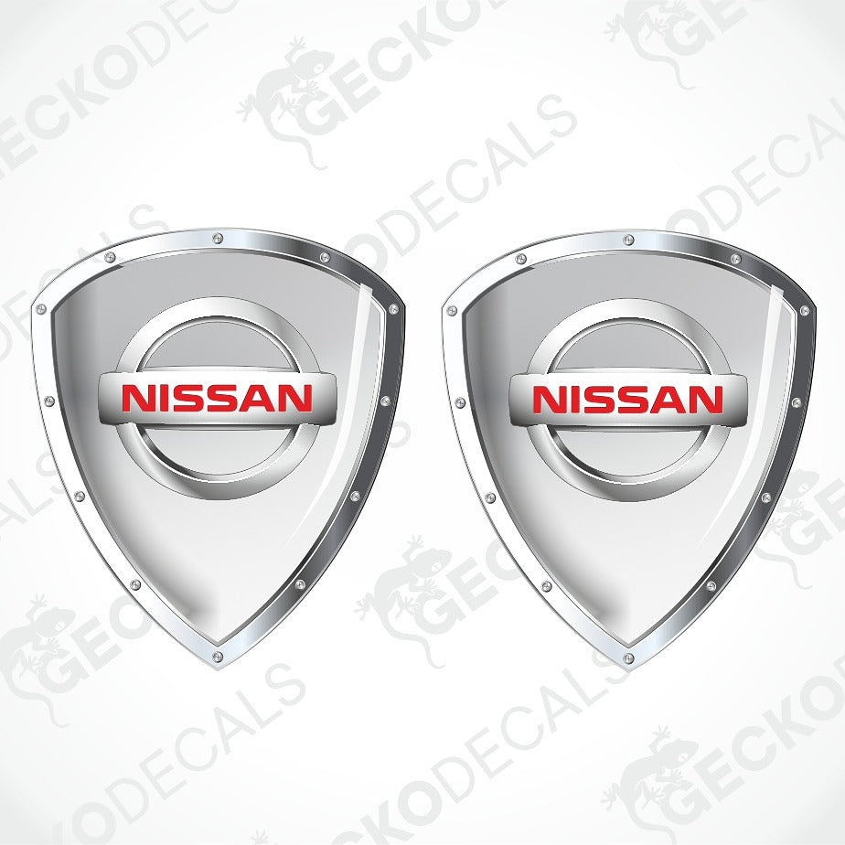 Two silver Nissan shield-shaped decal stickers with red NISSAN logos, shown on a light gray background with diagonal watermarks.