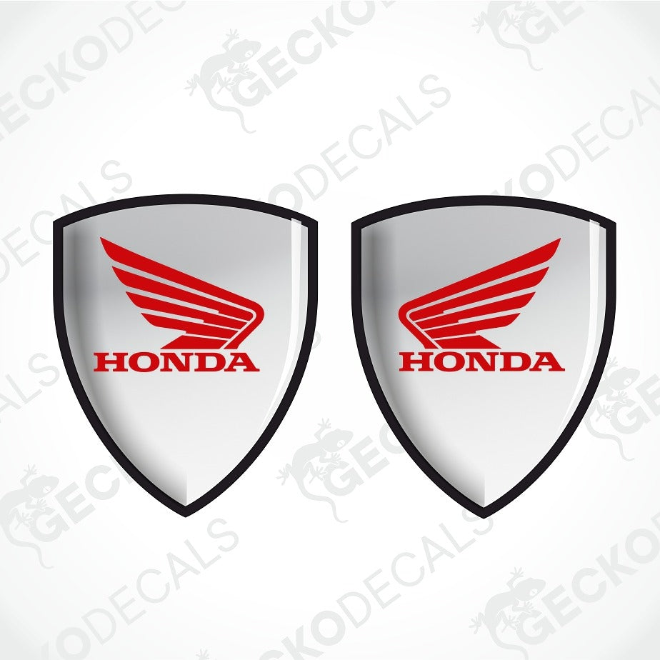 Two identical Honda shield-shaped decals on a light gray background with diagonal watermark text. Each decal has a silver-gray center, a red Honda wing logo, and red HONDA text outlined in black.